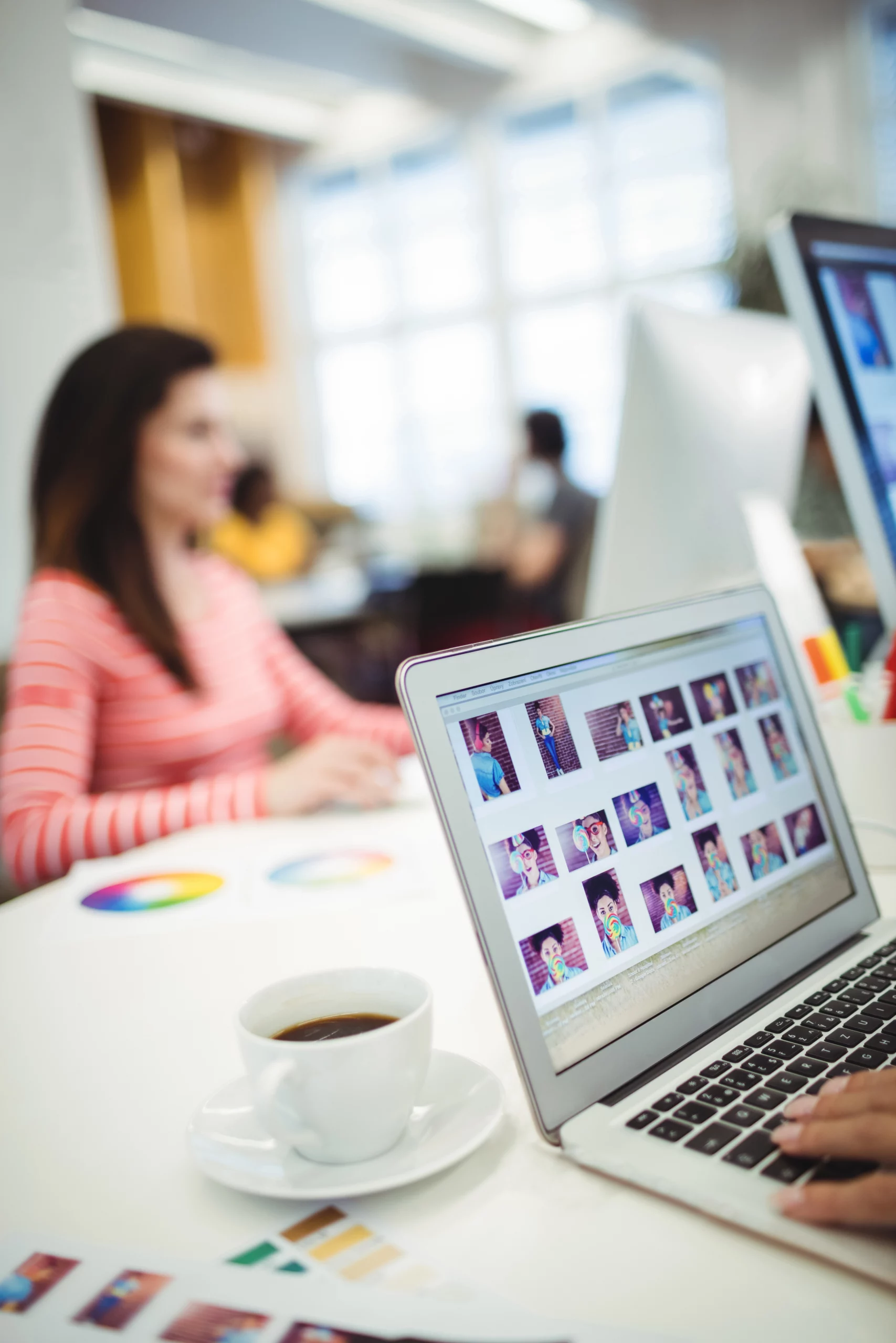 Équipe de création travaillant sur un site web sur-mesure avec un ordinateur portable affichant des images, une tasse de café et une personne en arrière-plan.
