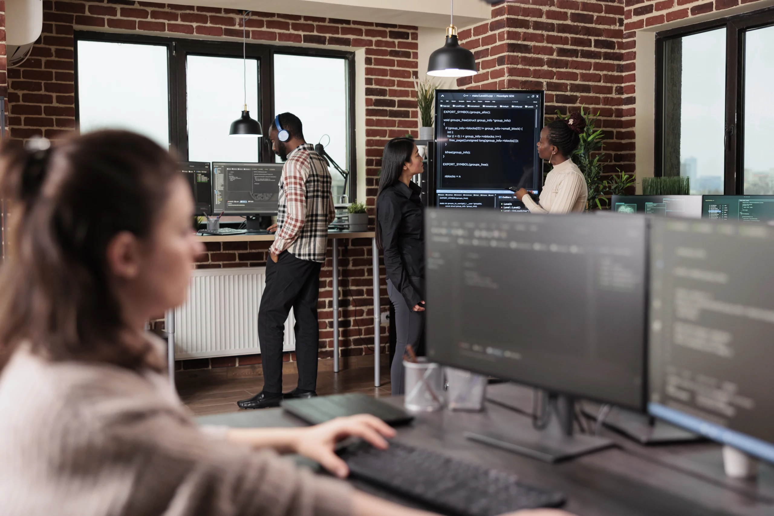 Équipe de développeurs web collaborant dans un bureau moderne avec plusieurs écrans et une présentation sur tableau numérique.