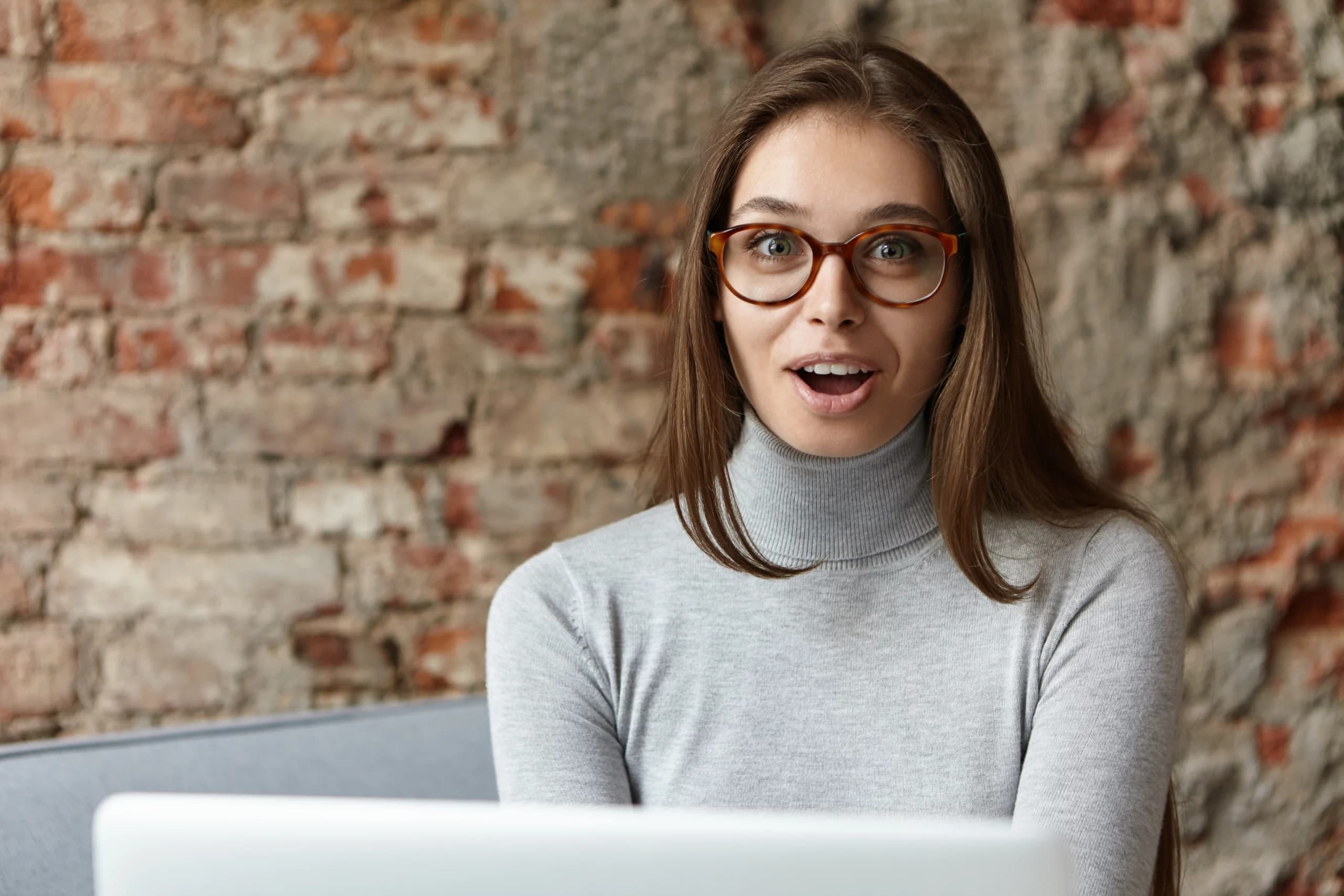 Femme avec des lunettes réagissant positivement devant un ordinateur portable, symbolisant les résultats d'une stratégie SEO réussie.