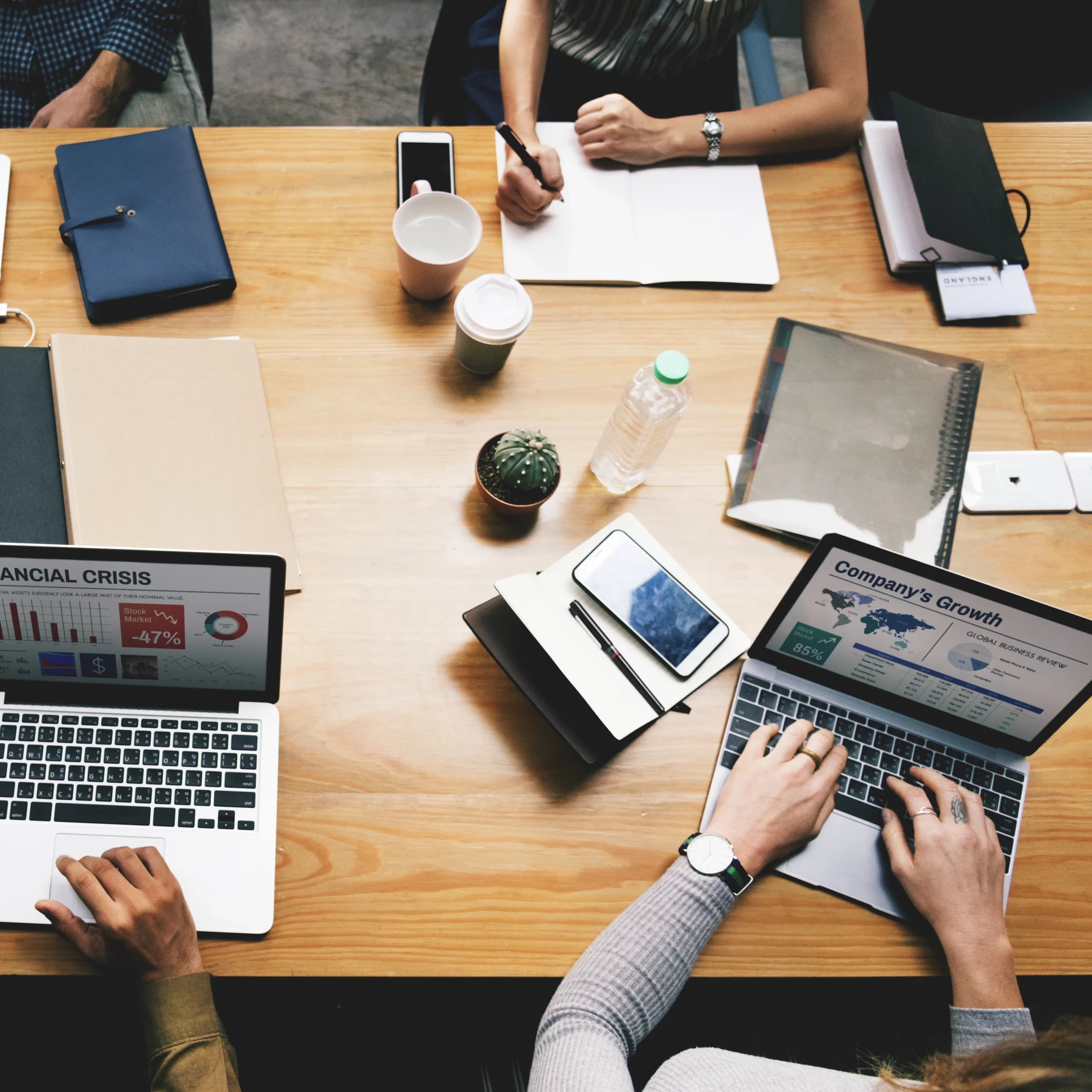 Réunion de collaborateurs travaillant sur un projet web avec des ordinateurs portables et des documents sur une table en bois.