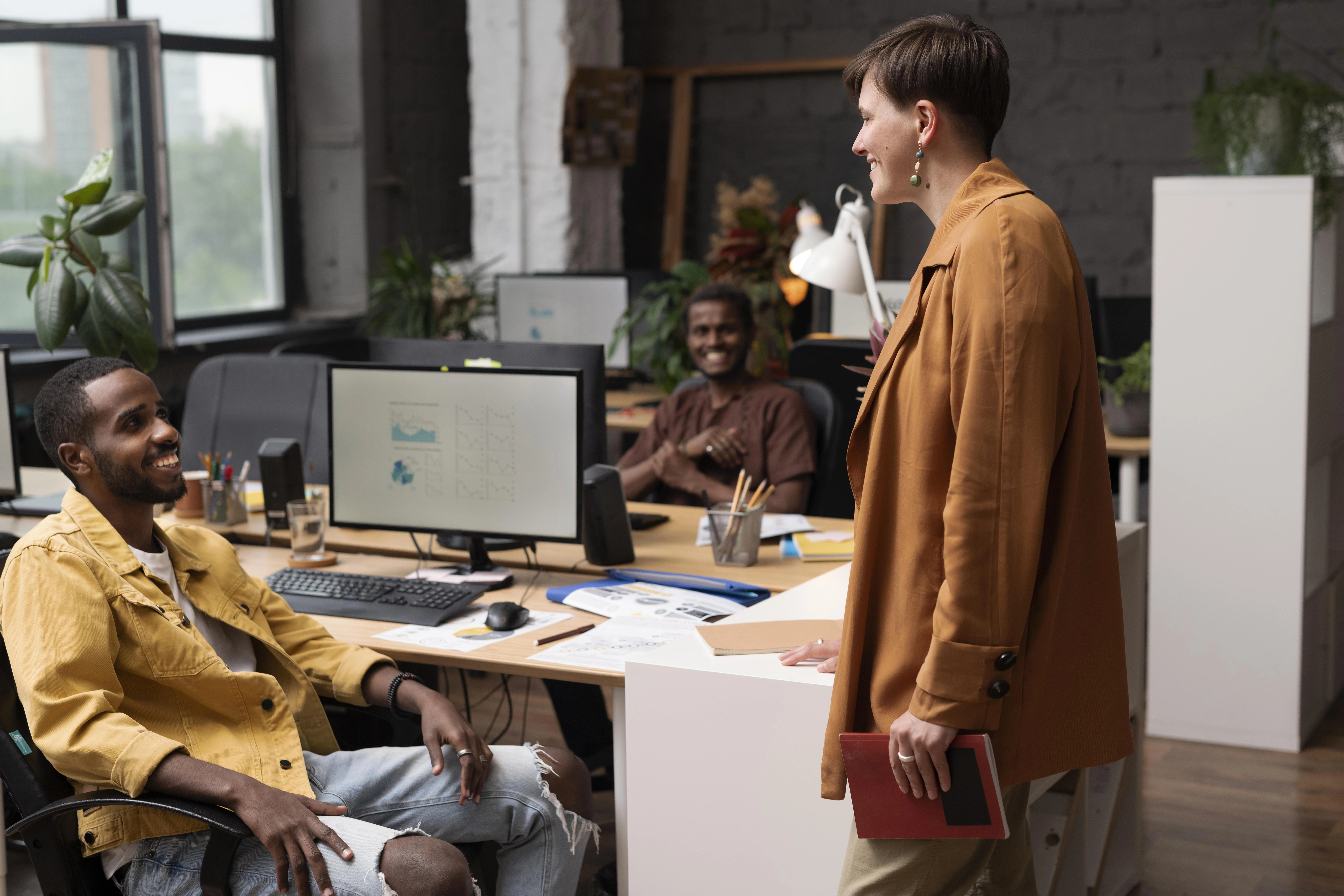 Un groupe de collègues discutant dans un bureau moderne et créatif, devant des écrans d'ordinateur.