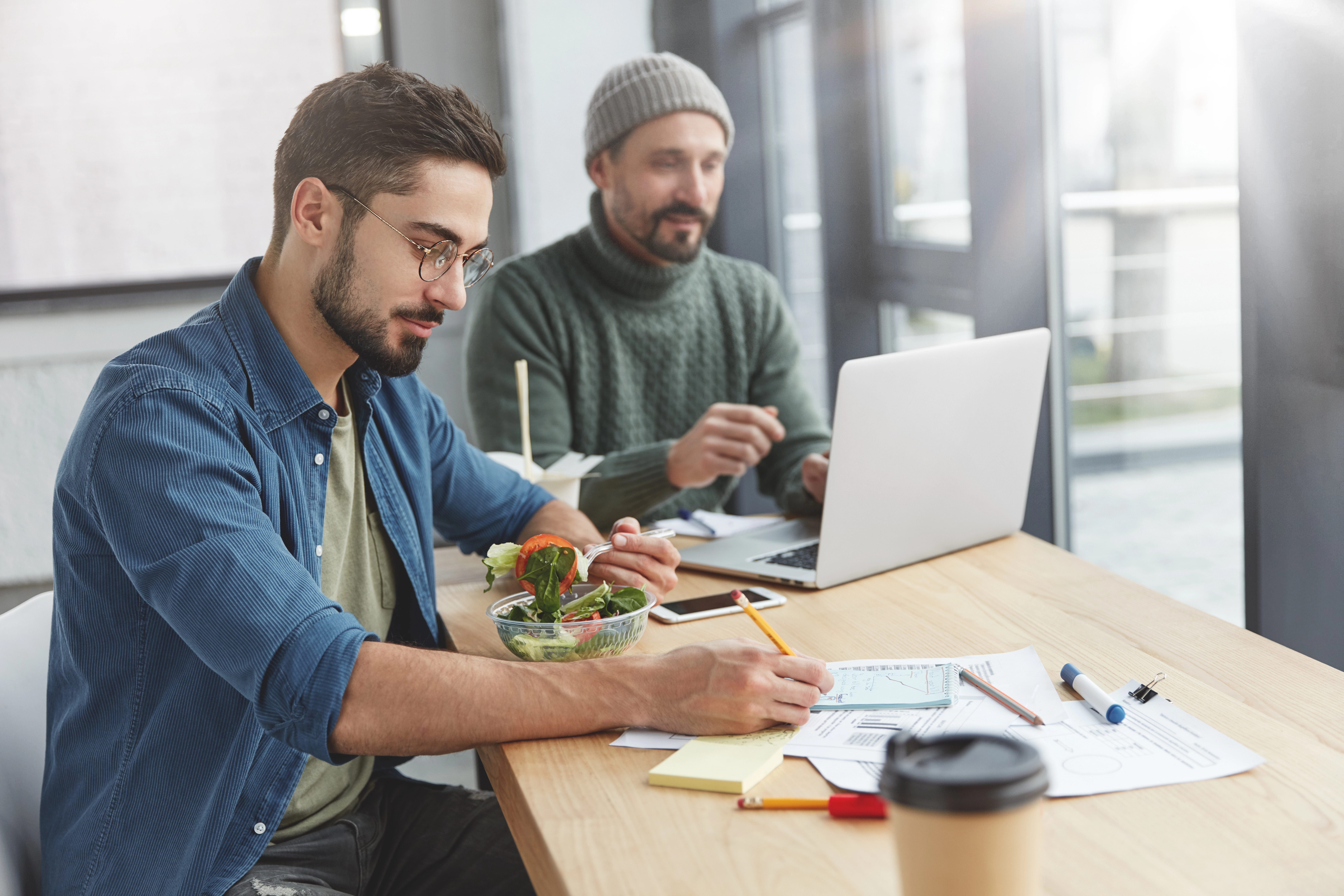 Deux hommes travaillant ensemble sur un projet de développement web sur-mesure, avec des documents et des ordinateurs portables.